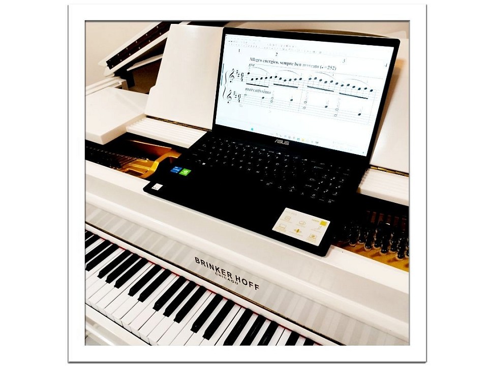 Ode to Joy on laptop on a white baby grand piano